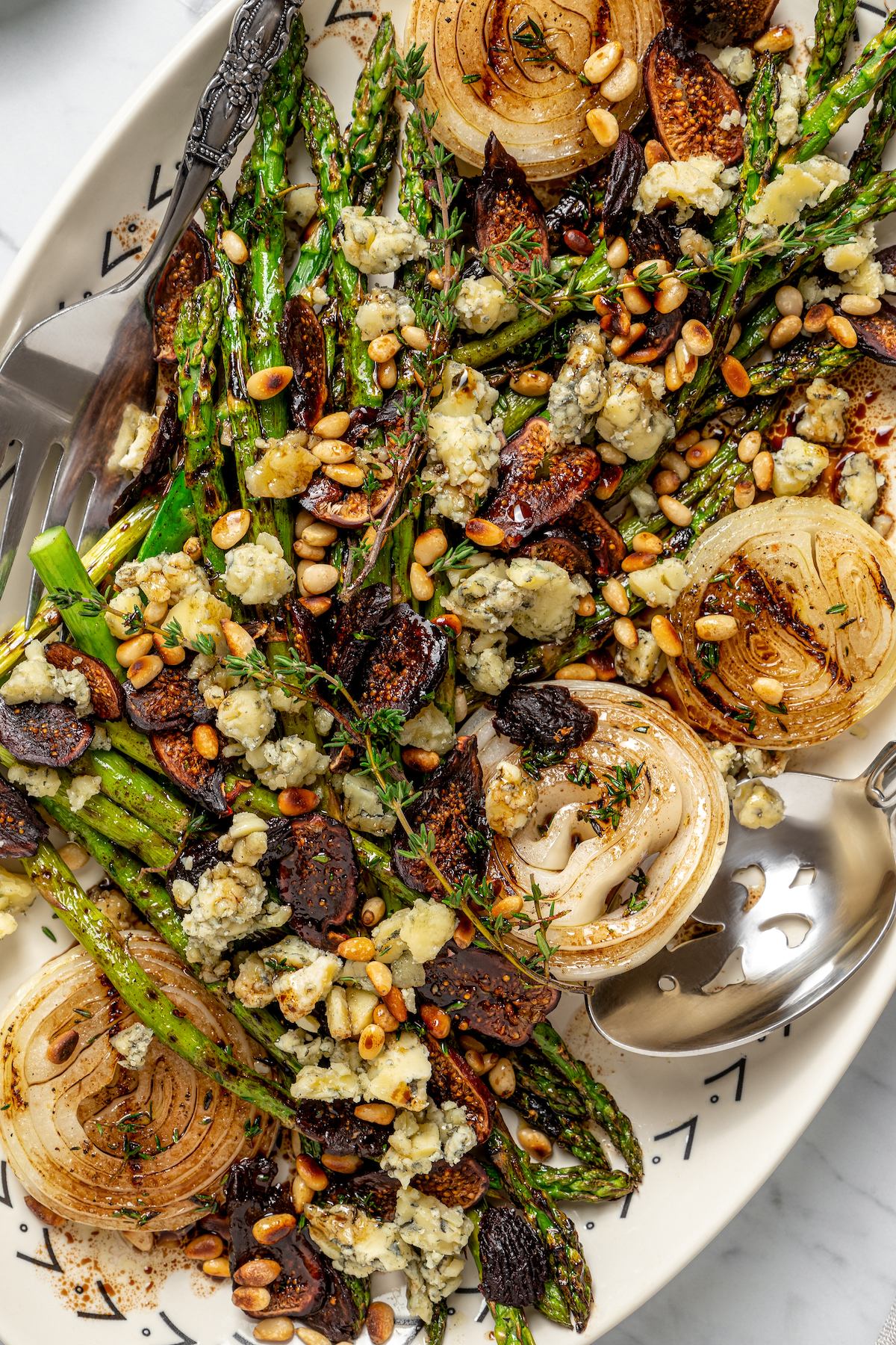 Grilled Asparagus with Onion recipe is topped with simple vinaigrette, blue cheese, black Mission figs, and toasted pine nuts. So flavorful! Close-up of asparagus and onion with blue cheese and other toppings.